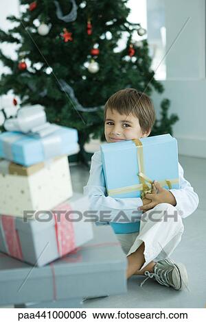 Boy sitting next to stack of Christmas presents, holding one against chest View Large Photo Image Stock Photograph - Boy sitting next to stack of Christmas presents, holding one against chest. Fotosearch
