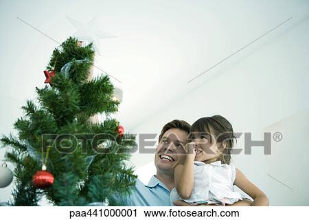 Stock Image - Father and daughter placing star on top of Christmas tree. Fotosearch