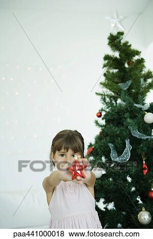 Girl holding out star decoration in front of Christmas tree View Large Photo Image Stock Photo - Girl holding out star decoration in front of Christmas tree. Fotosearch