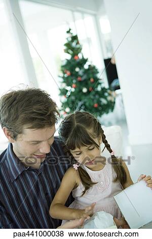 Girl sitting on father's lap, opening Christmas present View Large Photo Image Stock Photo - Girl sitting on father's lap, opening Christmas present. Fotosearch