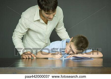 Father and son, man looking over boy's shoulder as he does homework View Large Photo Image Stock Photo - Father and son, man looking over boy's shoulder as he does homework. Fotosearch