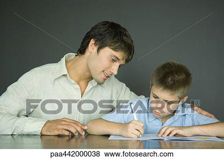 Father and son, man looking over boy's shoulder as he does homework View Large Photo Image Stock Photo - Father and son, man looking over boy's shoulder as he does homework. Fotosearch