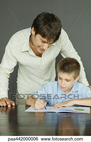 Stock Photograph - Father and son, man looking over boy's shoulder as he colors. Fotosearch