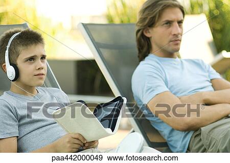 Father and son sitting on lounge chairs together, boy listening to headphones View Large Photo Image Stock Photo - Father and son sitting on lounge chairs together, boy listening to headphones. Fotosearch
