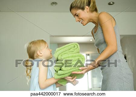 Stock Photo - Mother and daughter, girl handing woman stack of towels. Fotosearch