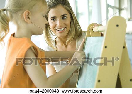 Mother and daughter together as girl draws on chalkboard View Large Photo Image Stock Photo - Mother and daughter together as girl draws on chalkboard. Fotosearch