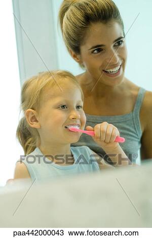 Stock Image - Mother and daughter together while girl brushes teeth. Fotosearch