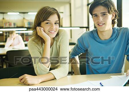 College students sitting at table in library, smiling at camera View Large Photo Image Picture - College students sitting at table in library, smiling at camera. Fotosearch