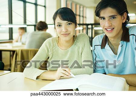 Stock Photography - College students sitting at table in library, smiling at camera. Fotosearch