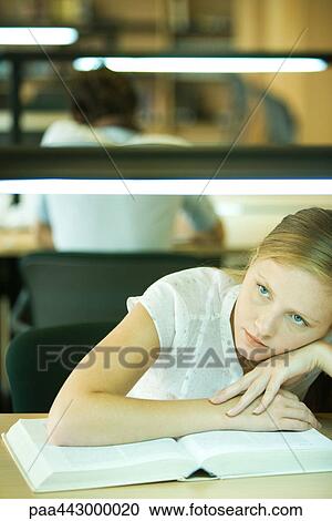 Female college student sitting at table in library, resting on book View Large Photo Image Stock Image - Female college student sitting at table in library, resting on book. Fotosearch