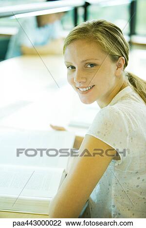 Female college student sitting at table in library, smiling at camera View Large Photo Image Stock Image - Female college student sitting at table in library, smiling at camera. Fotosearch