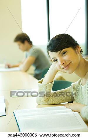 Female college student sitting at table with book, smiling at camera View Large Photo Image Stock Photography - Female college student sitting at table with book, smiling at camera. Fotosearch