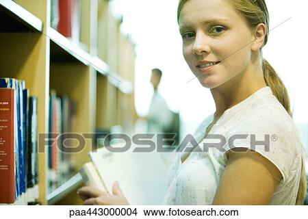 Female college student standing by shelves in library View Large Photo Image Picture - Female college student standing by shelves in library. Fotosearch