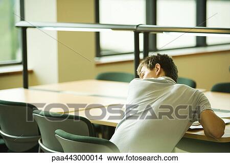Picture - Male college student sitting at table, looking over shoulder. Fotosearch