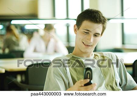 Male college student sitting in study room, looking at cell phone, smiling View Large Photo Image Stock Image - Male college student sitting in study room, looking at cell phone, smiling. Fotosearch