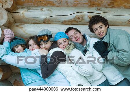 Stock Photograph - Young friends standing by log cabin, leaning on each other, portrait. Fotosearch