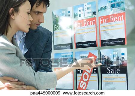 Couple looking at properties in window of real estate agency View Large Photo Image Stock Photo - Couple looking at properties in window of real estate agency. Fotosearch