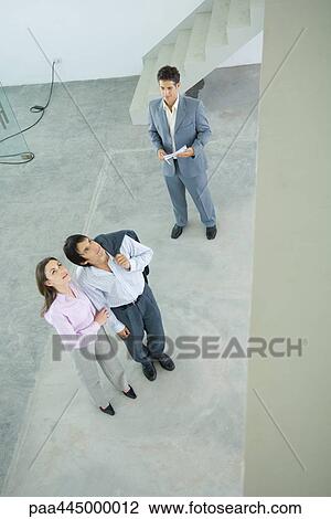 Male real estate agent standing in home interior with young couple, full length, high angle view View Large Photo Image Stock Image - Male real estate agent standing in home interior with young couple, full length, high angle view. Fotosearch