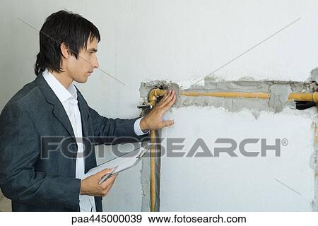 Stock Photo - Man in suit inspecting pipes in wall. Fotosearch