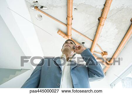 Man in suit using cell phone, bare pipes overhead, low angle view View Large Photo Image Stock Photo - Man in suit using cell phone, bare pipes overhead, low angle view. Fotosearch