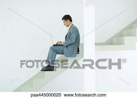 Stock Image - Man sitting on stairs, using laptop. Fotosearch