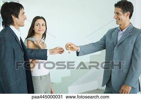 Stock Image - Real estate agent handing keys to young couple. Fotosearch