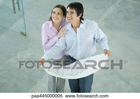 Stock Photography - Young couple holding blueprints, smiling. Fotosearch