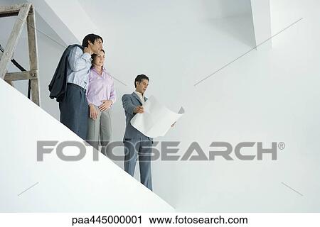 Young couple standing with architect, overlooking spacious interior View Large Photo Image Stock Image - Young couple standing with architect, overlooking spacious interior. Fotosearch