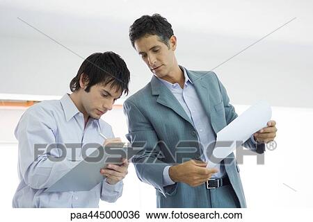 Young man writing on clipboard, mature man looking over shoulder View Large Photo Image Stock Photograph - Young man writing on clipboard, mature man looking over shoulder. Fotosearch