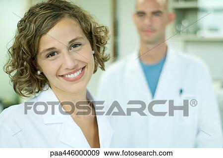 Stock Photo - Female doctor smiling, male colleague in background, portrait. Fotosearch