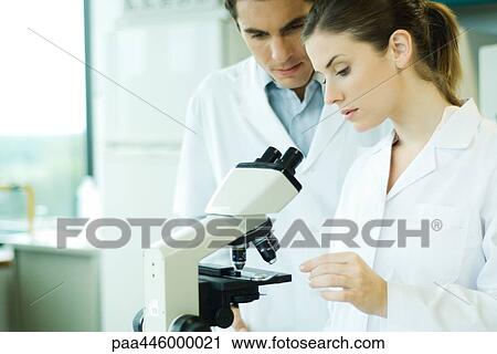 Male and female scientist standing by microscope View Large Photo Image Stock Image - Male and female scientist standing by microscope. Fotosearch