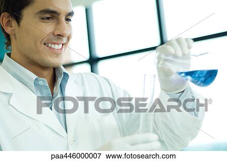 Stock Photo - Male scientist transfering liquid from flask to cylinder, smiling. Fotosearch