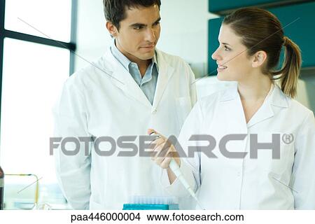 Picture - Young female lab worker smiling at supervisor. Fotosearch