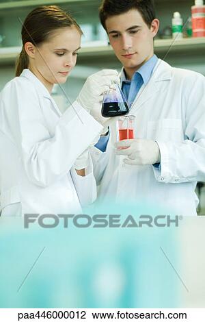 Stock Image - Young male and female lab workers, holding lab glassware. Fotosearch