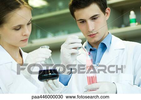 Stock Image - Young male and female lab workers, holding lab glassware. Fotosearch