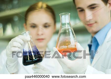 Stock Image - Young male and female lab workers, holding lab glassware. Fotosearch