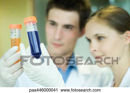 Stock Image - Young male and female lab workers, holding up test tubes. Fotosearch
