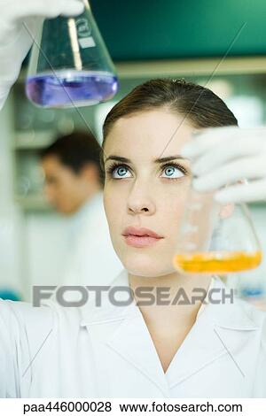 Stock Photo - Young woman in research lab, holding up two flasks. Fotosearch