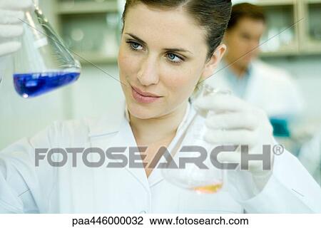Stock Image - Young woman working in scientific laboratory, holding up flasks. Fotosearch
