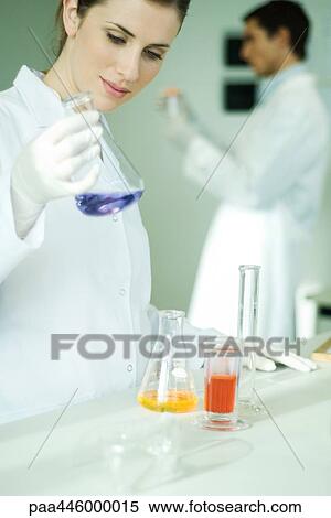 Stock Photography - Young woman working in scientific laboratory, picking up flask. Fotosearch