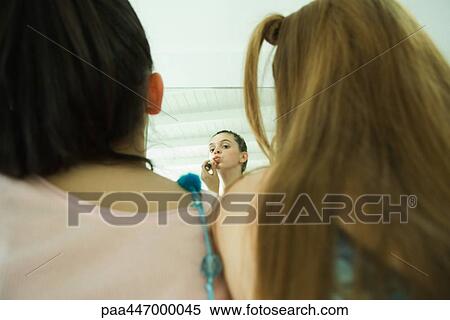Rear view of two young friends, one looking at self in mirror, applying lipstick View Large Photo Image Stock Photography - Rear view of two young friends, one looking at self in mirror, applying lipstick . Fotosearch