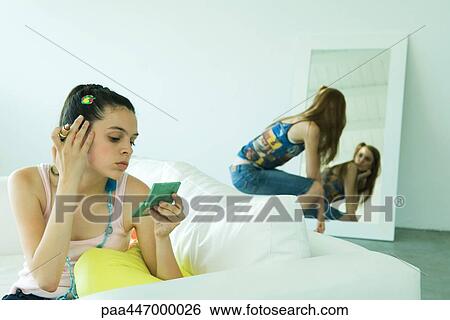 Teenage girl holding lipstick, looking at self in hand mirror, friend in background View Large Photo Image Stock Photograph - Teenage girl holding lipstick, looking at self in hand mirror, friend in background. Fotosearch