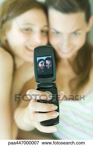 Stock Photo - Teenage girl photographing self with friend using cell phone. Fotosearch