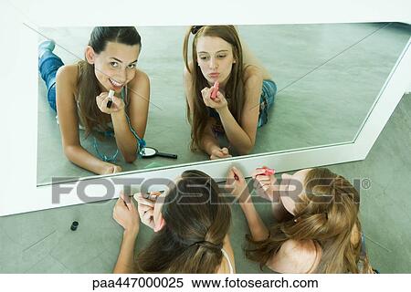 Two friends lying on ground, applying lipstick, looking in mirror, one looking at camera View Large Photo Image Stock Photography - Two friends lying on ground, applying lipstick, looking in mirror, one looking at camera. Fotosearch