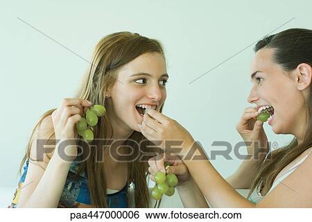 Two young friends feeding each other grapes, smiling View Large Photo Image Stock Photograph - Two young friends feeding each other grapes, smiling. Fotosearch