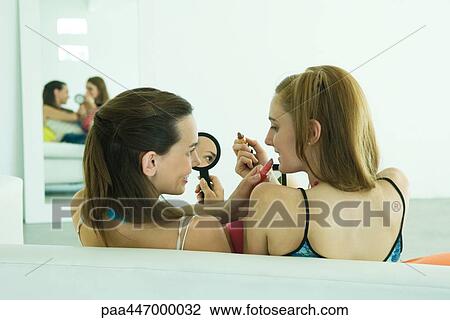 Two young friends holding up lipstick, looking at each other, smiling, rear view View Large Photo Image Stock Image - Two young friends holding up lipstick, looking at each other, smiling, rear view. Fotosearch