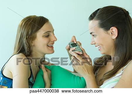 Two young friends looking at cell phone together, smiling View Large Photo Image Stock Photo - Two young friends looking at cell phone together, smiling. Fotosearch