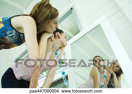 Picture - Two young friends looking at selves in mirror, puckering mouths, one leaning on the other's shoulder. Fotosearch
