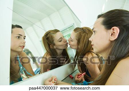 Two young friends looking at selves in mirror, one kissing her reflection View Large Photo Image Stock Photo - Two young friends looking at selves in mirror, one kissing her reflection. Fotosearch
