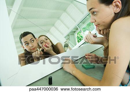 Two young friends looking at selves in mirror, one applying lipstick View Large Photo Image Stock Photograph - Two young friends looking at selves in mirror, one applying lipstick. Fotosearch